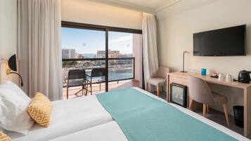 Habitación de hotel con cama, escritorio, silla, televisor y balcón con vista a la ciudad.