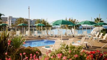 Uma área à beira da piscina com espreguiçadeiras e guarda-sóis, cercada por vegetação e uma vista desobstruída do oceano.