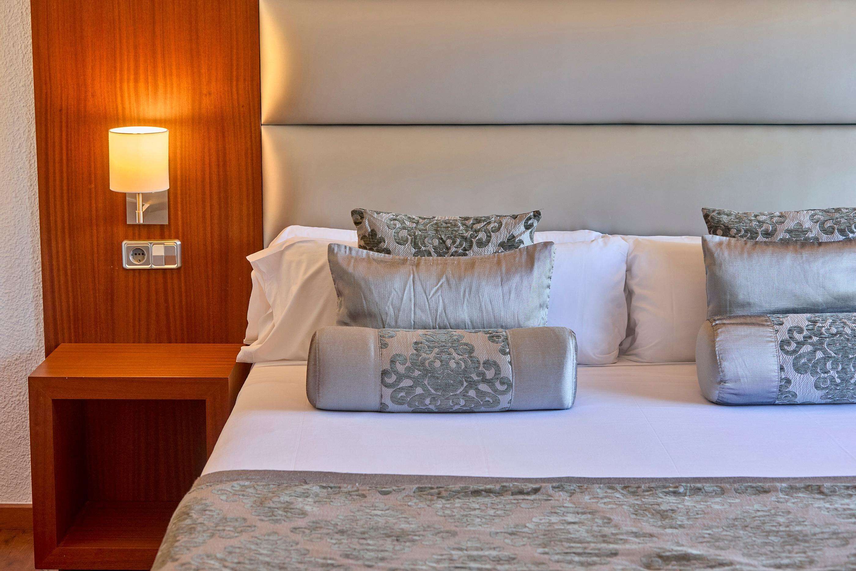 A neatly made bed with patterned pillows and a bedside table with a lamp.