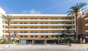 A multi-story hotel with a flat facade, balconies, and a parking area with bicycles.