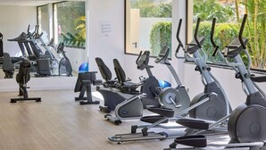 Un gimnasio con diferentes máquinas de ejercicio, ventanas amplias y vistas al exterior a zonas verdes.