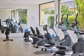 Un gimnasio con diferentes máquinas de ejercicio, ventanas amplias y vistas al exterior a zonas verdes.