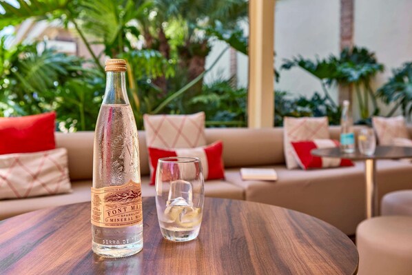 A bottle of Font Major Sparkling Mineral Water and a glass on a wooden table in a cozy indoor setting with a sofa and cushions in the background. - Zafiro Rey Don Jaime (Calvia)