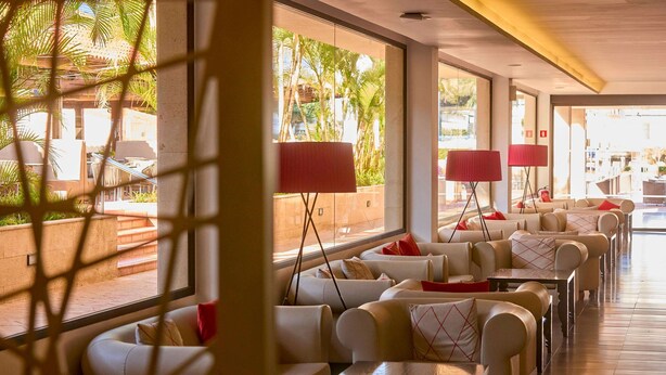 Un hall de hotel con zonas de estar, ventanas amplias y lámparas rojas.