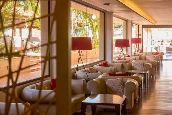 Un hall de hotel con zonas de estar, ventanas amplias y lámparas rojas.