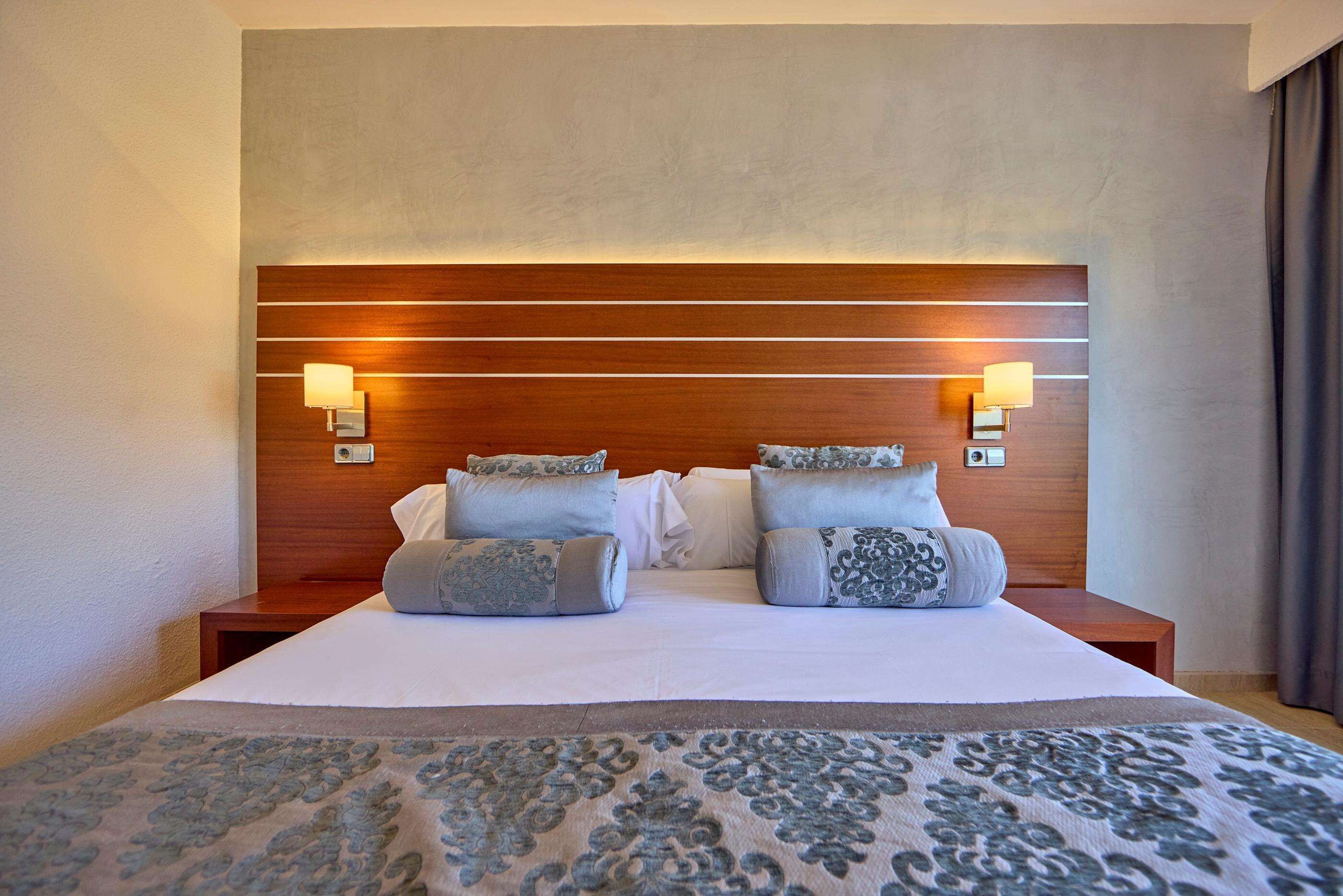 Ein Hotelzimmer mit einem großen Bett, zwei Nachttischlampen und einem Kopfteil mit horizontalen Linien.
