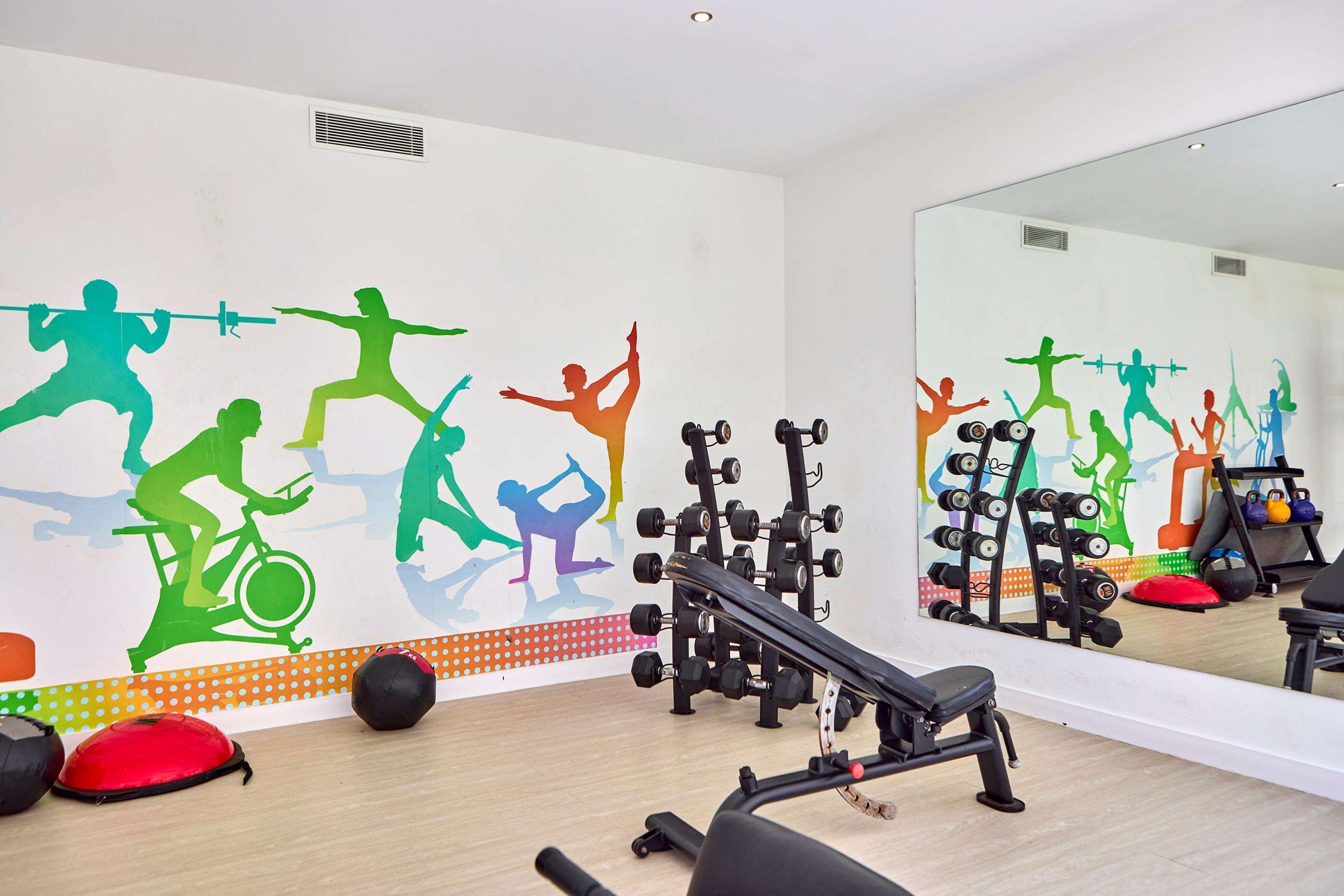 Une salle de sport équipée de matériel d’exercice, dotée d’un miroir et agrémentée d’œuvres d’art murales aux couleurs vives.