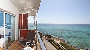Un balcon avec vue sur la mer, un lit avec une literie bleue et une chaise.