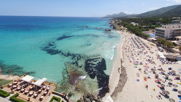 Une plage aux eaux turquoise et limpides, un rivage sablonneux et un restaurant doté d’une terrasse offrant une vue sur la mer.