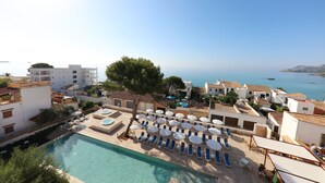 Un espace piscine doté de chaises longues et de parasols, offrant une vue sur la côte.