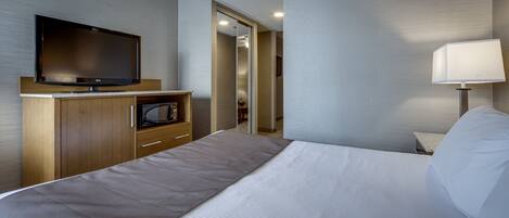 A hotel room with a bed, a television, a microwave, a lamp, and a mirror.