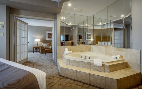 A hotel room with a large bathtub, a television, a sofa, and a dining area.