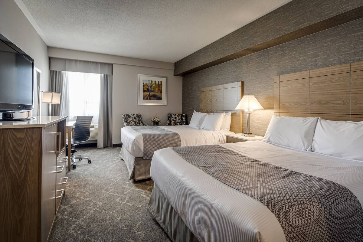 A hotel room with two beds, a desk with a TV, a lamp, and a painting on the wall.