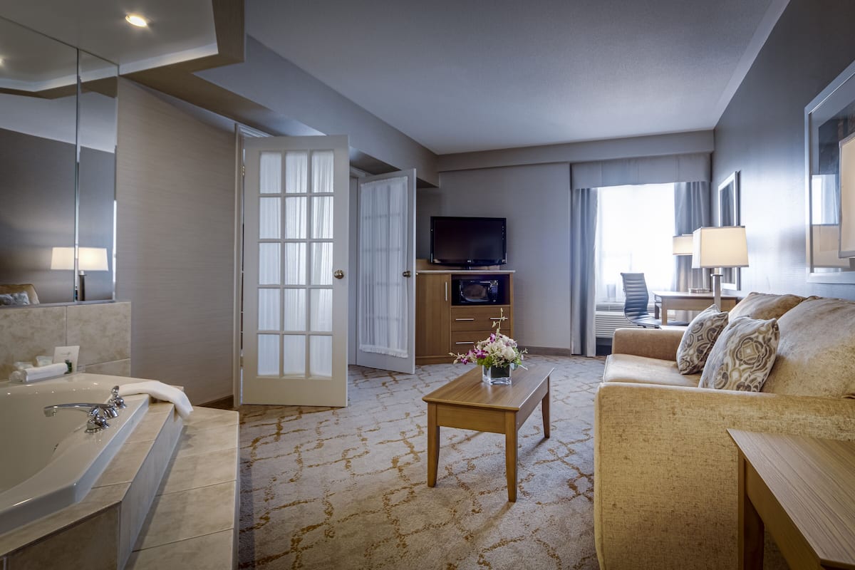 A hotel room with a bathroom, a sofa, a coffee table, a TV, and a desk.