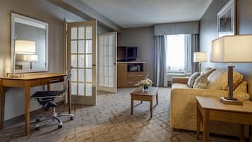 A hotel room with a desk, chair, sofa, and a television.