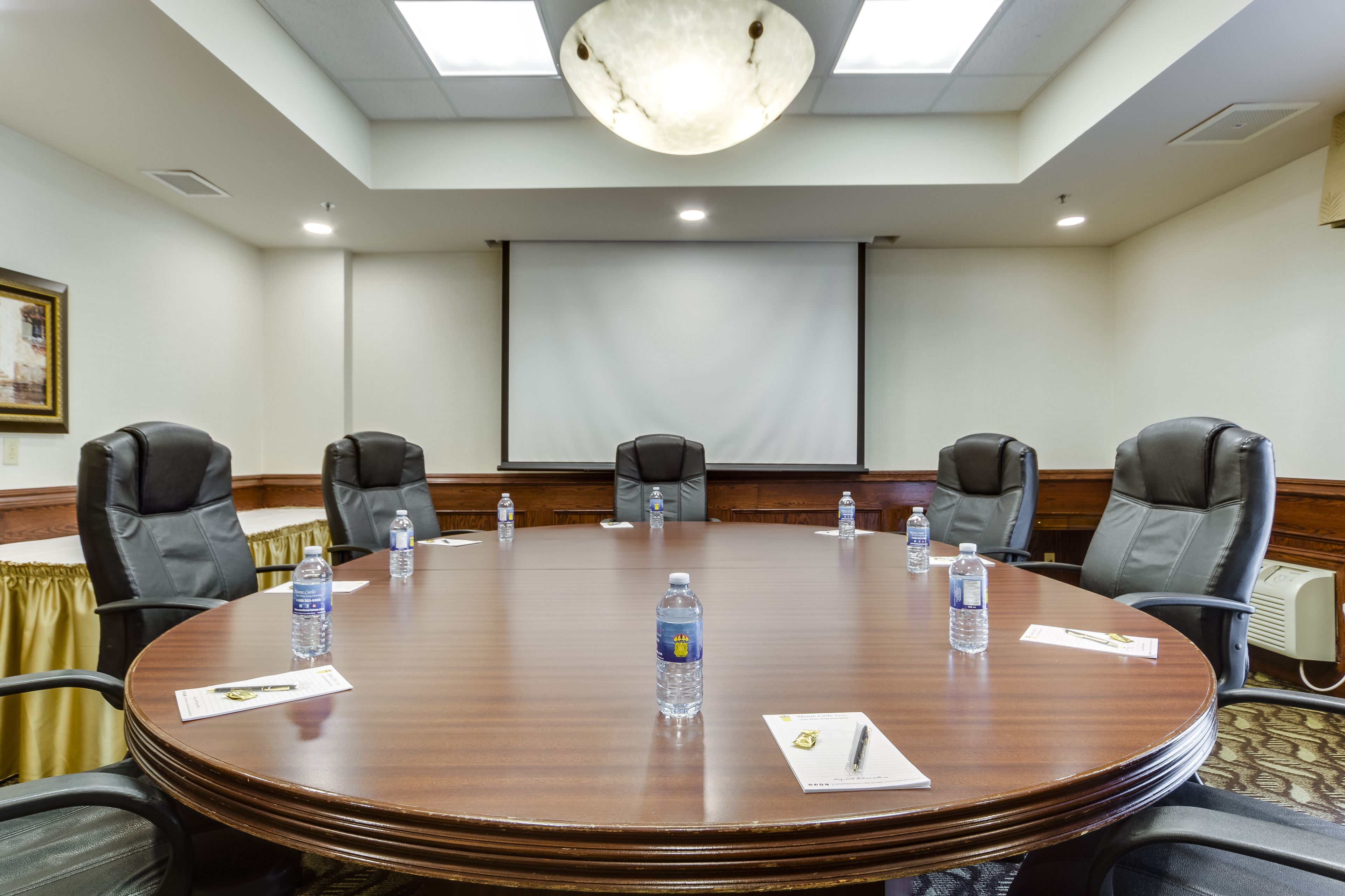Una sala de conferencias con una mesa redonda, seis sillas, botellas de agua y documentos.