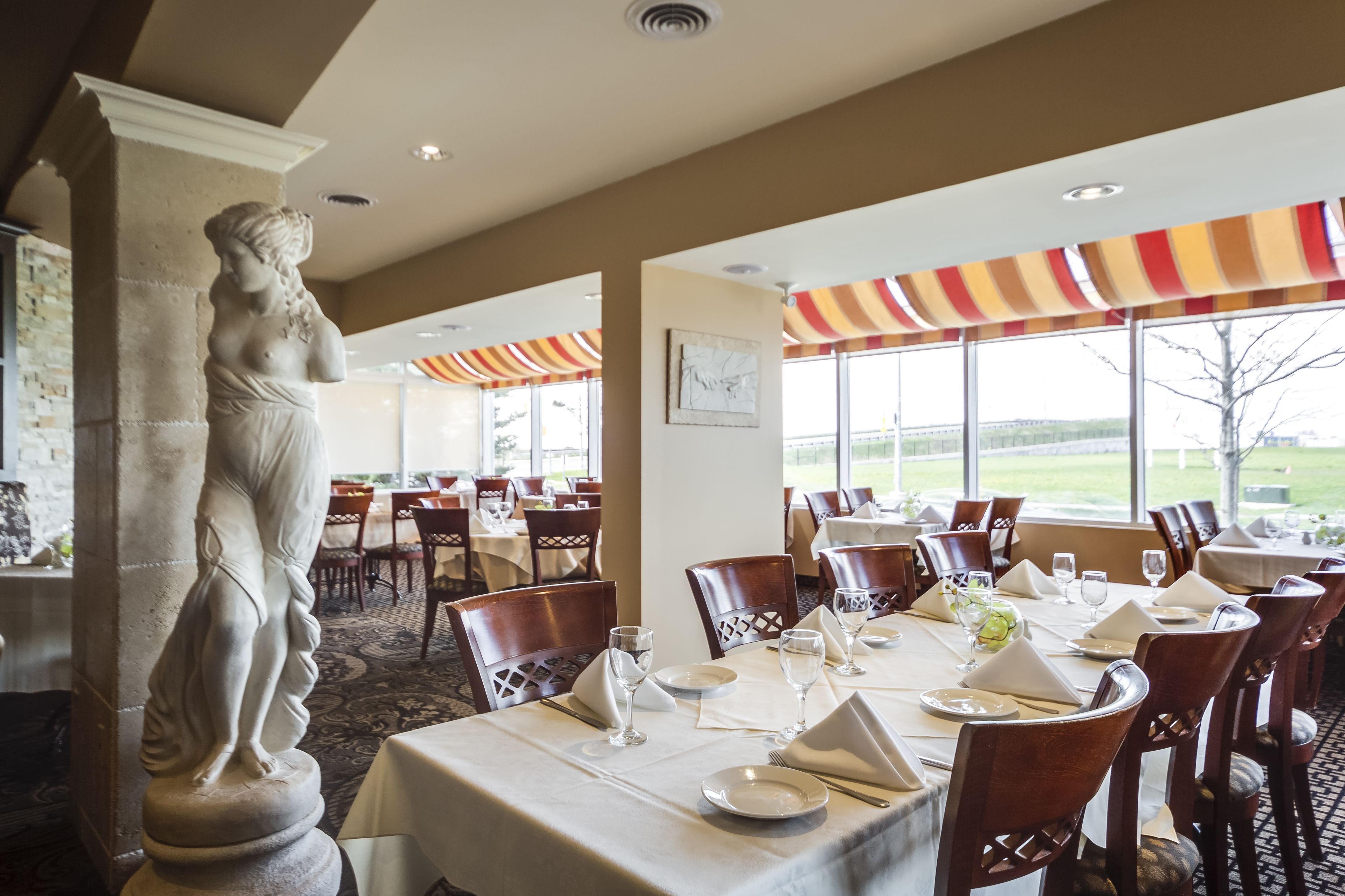 A dining area with tables set for service, a statue, and large windows with a view.