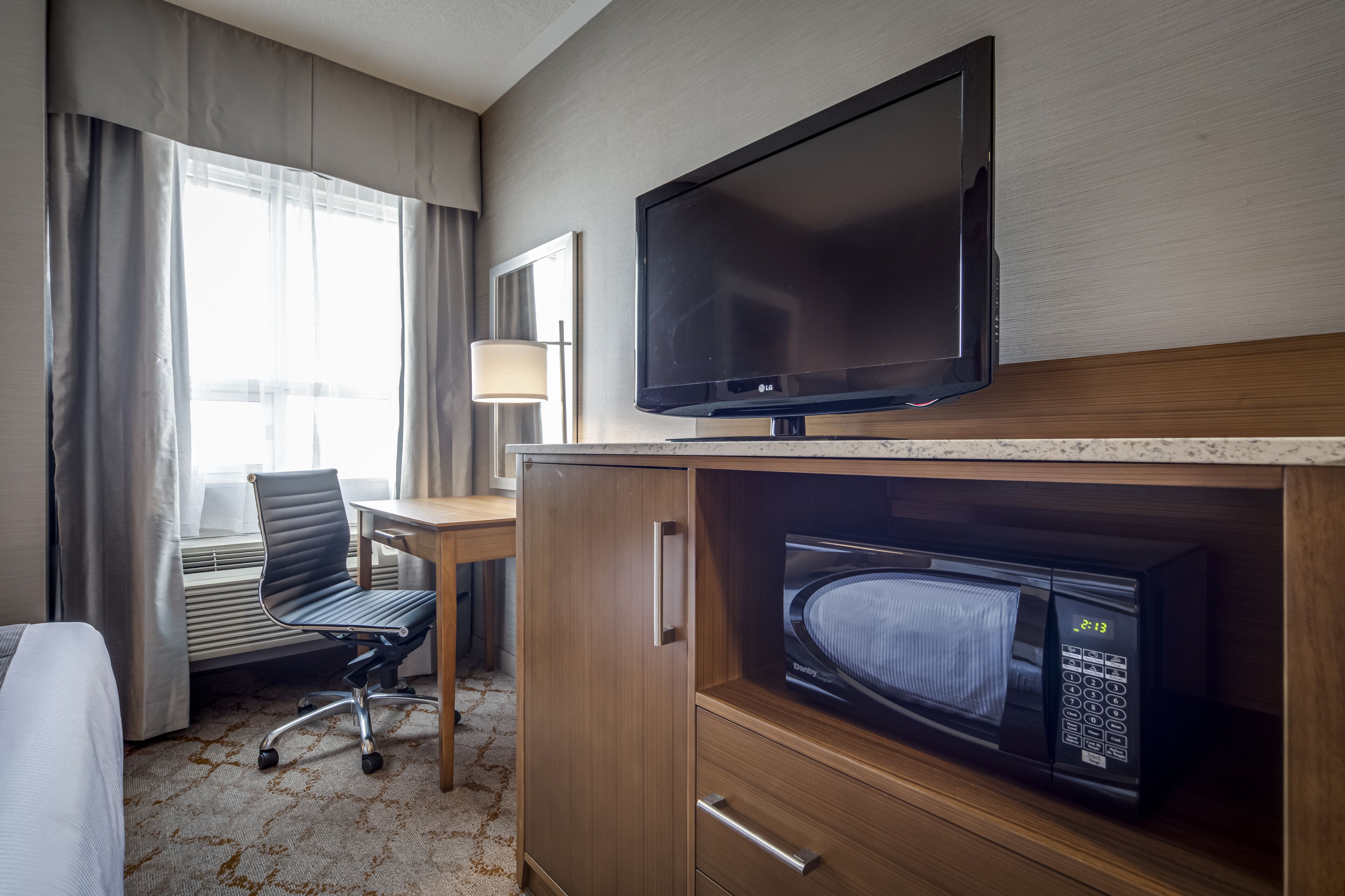Una habitación de hotel con televisión, microondas, escritorio y silla.