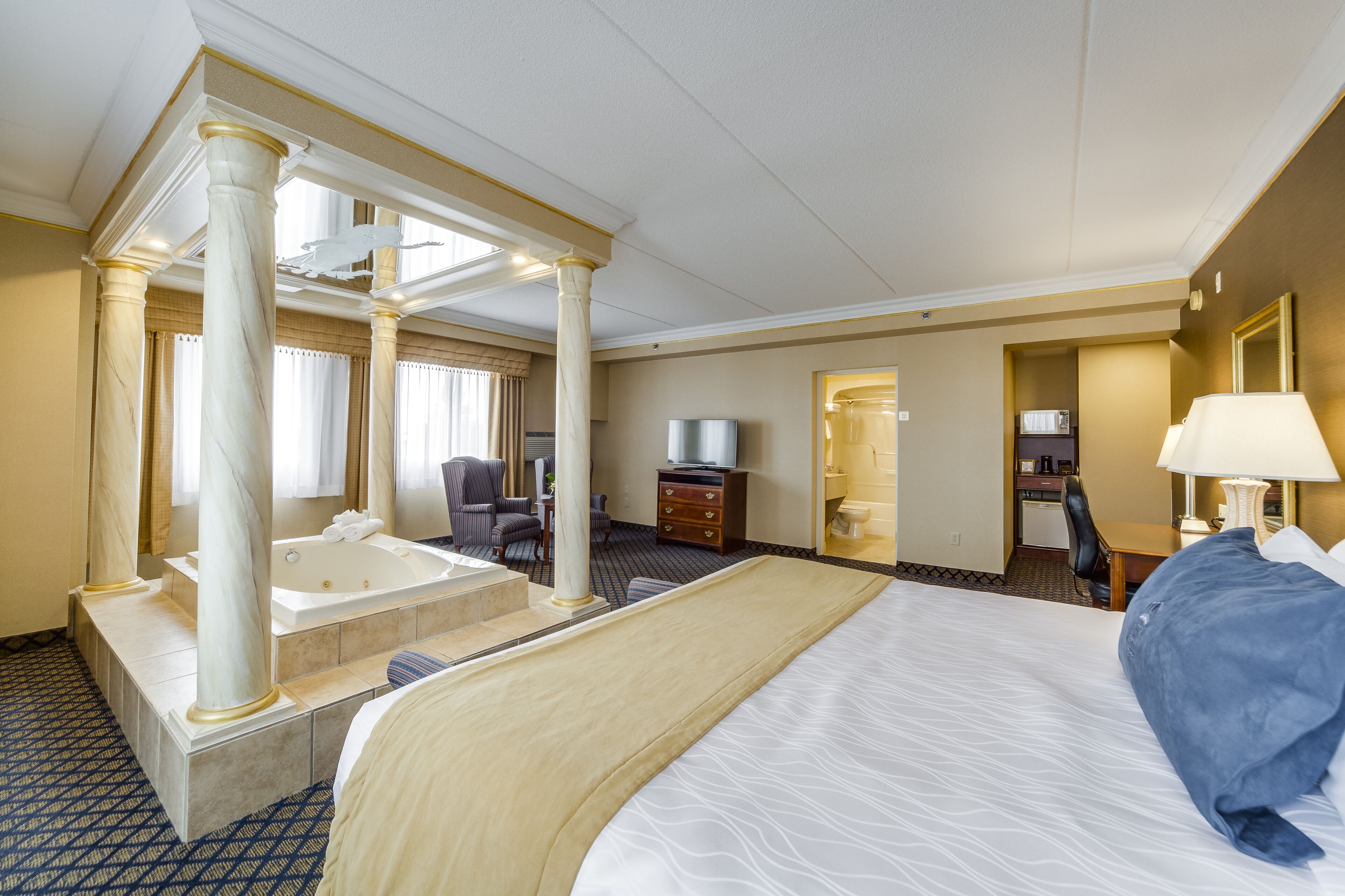 Habitación de hotel con una cama grande, una zona de estar separada con una silla y una mesa, una bañera y un escritorio con lámpara.