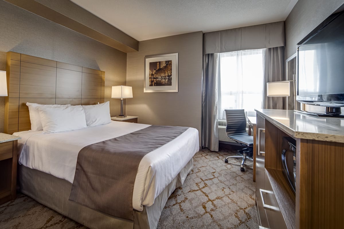 A hotel room with a large bed, a desk with a chair, a television, and a window with curtains.