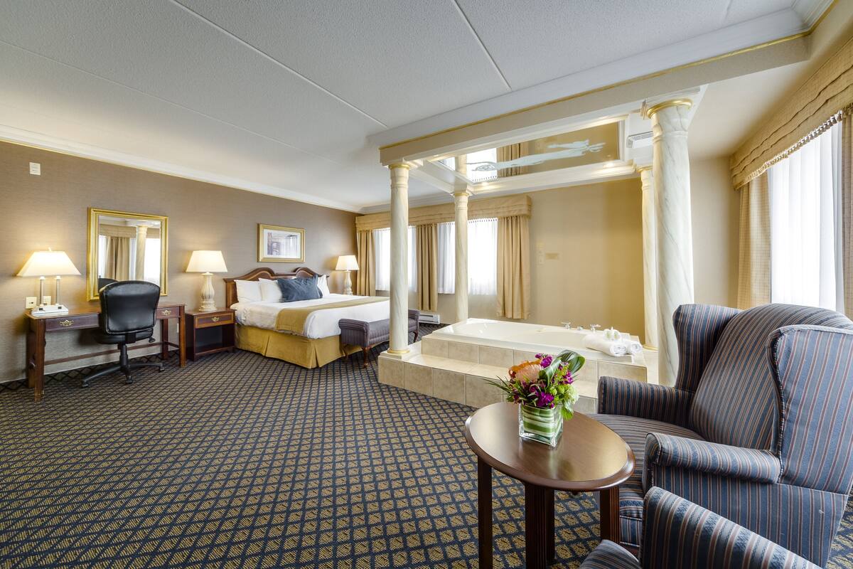 Quarto de hotel com uma cama grande, área de estar com uma poltrona e uma mesa, banheira e escrivaninha com cadeira.