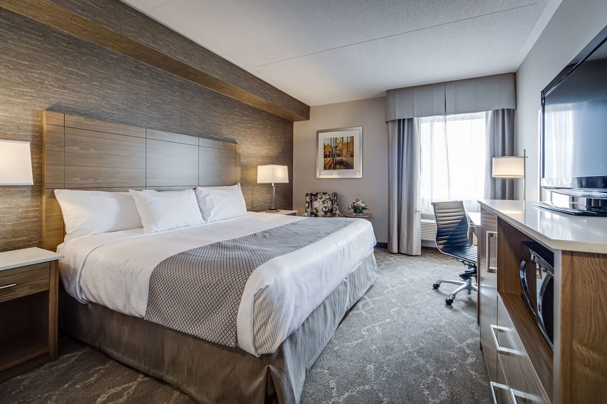 Quarto de hotel com uma cama grande, uma escrivaninha com televisão, uma cadeira e um quadro na parede.