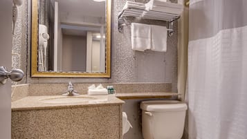 Un baño con lavamanos de encimera de granito, inodoro blanco, toallero con dos toallas, espejo con marco dorado y cortina de ducha.