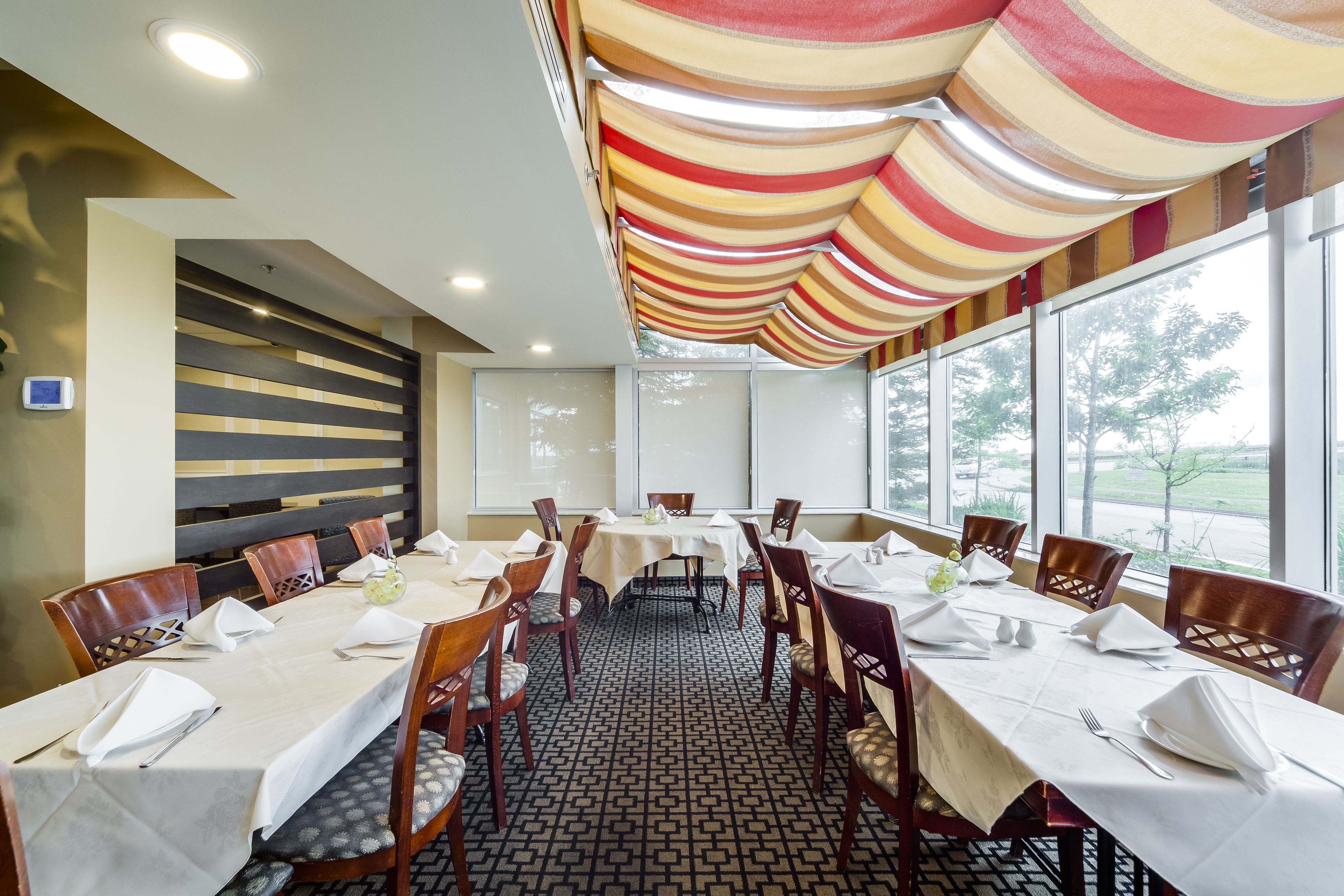 A dining area with tables set for six, wooden chairs, and a patterned floor.