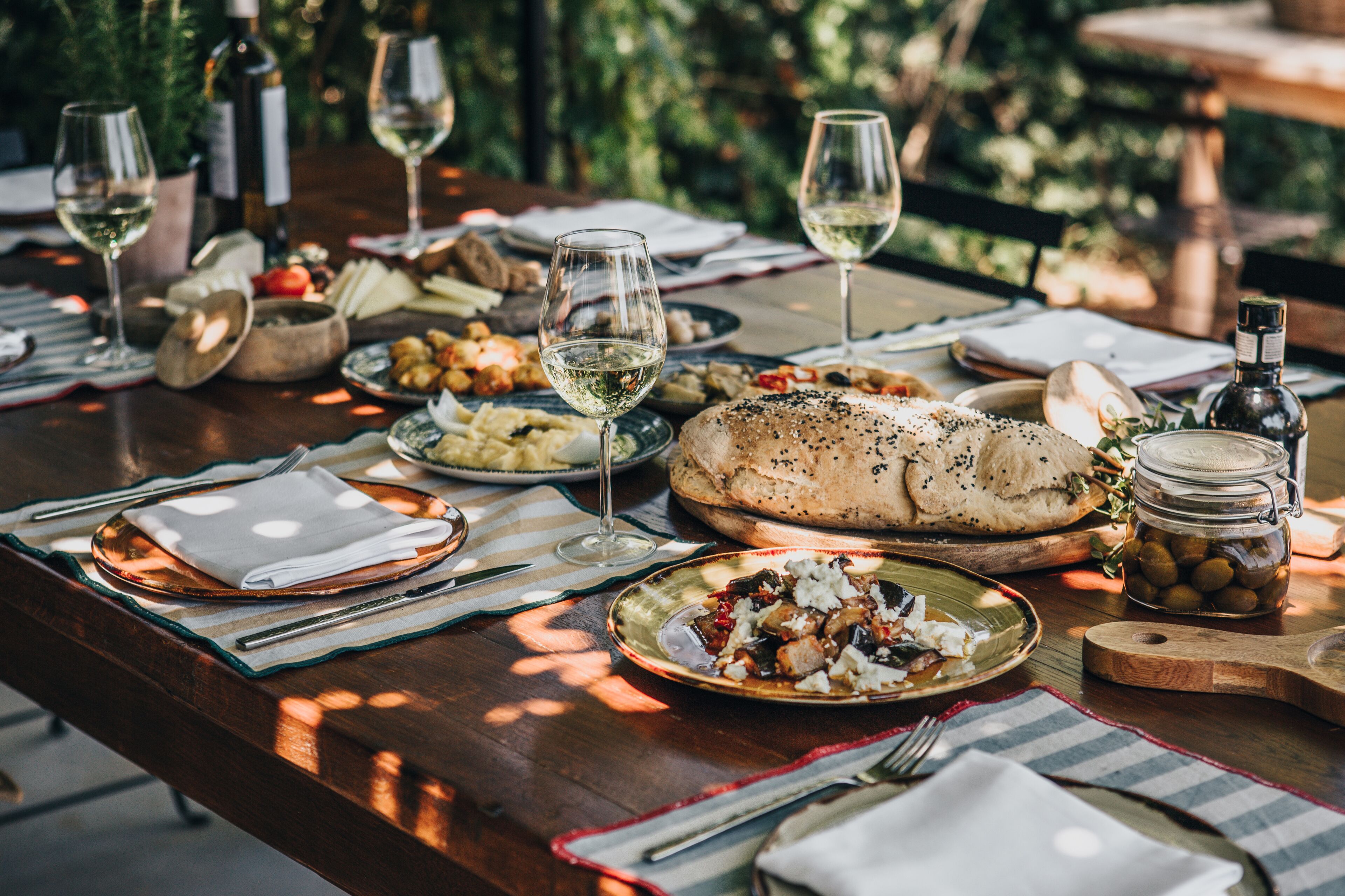 A wooden dining table set with plates, glasses, and a loaf of bread.