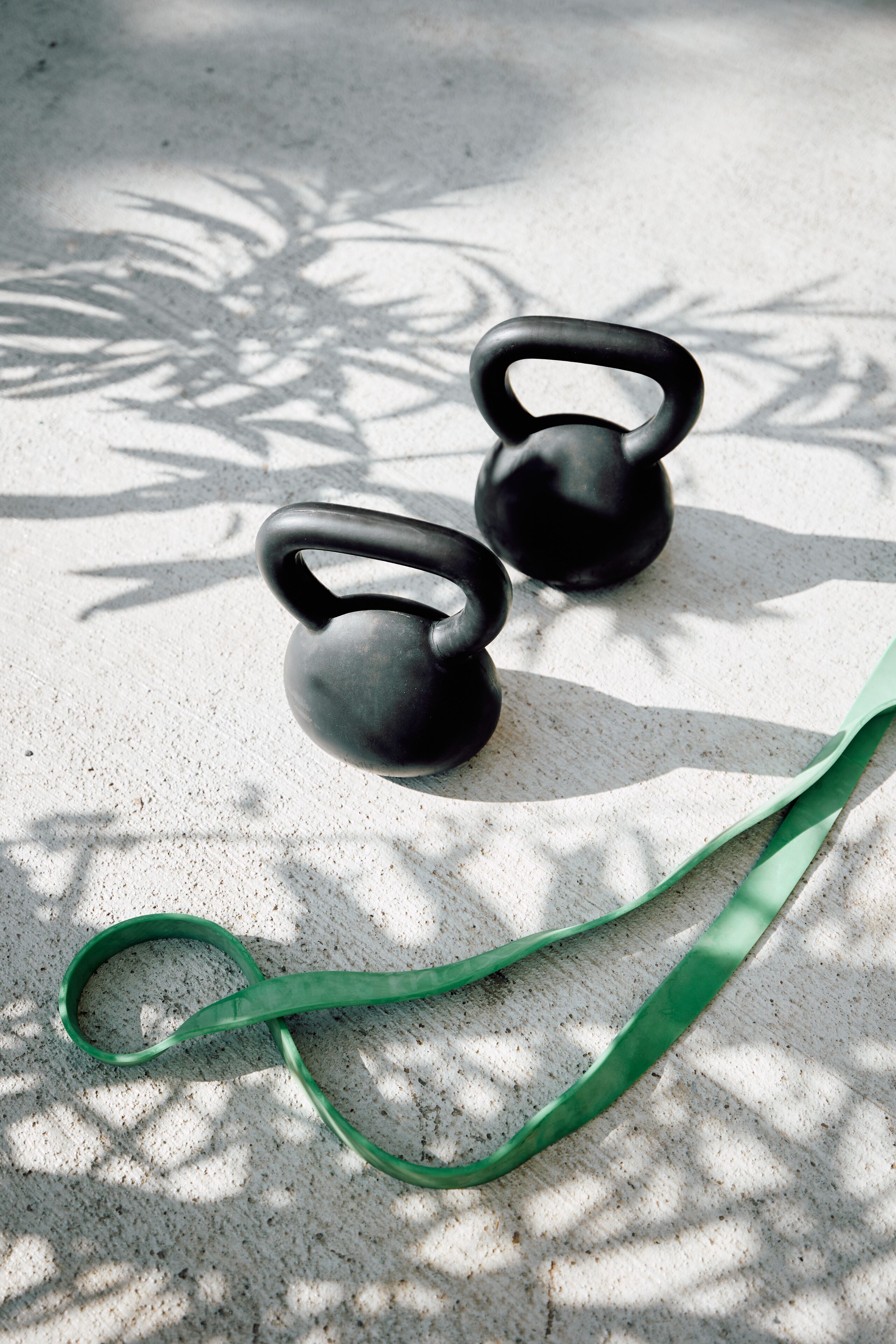 Two kettlebells and a green resistance band on a textured surface with shadows.
