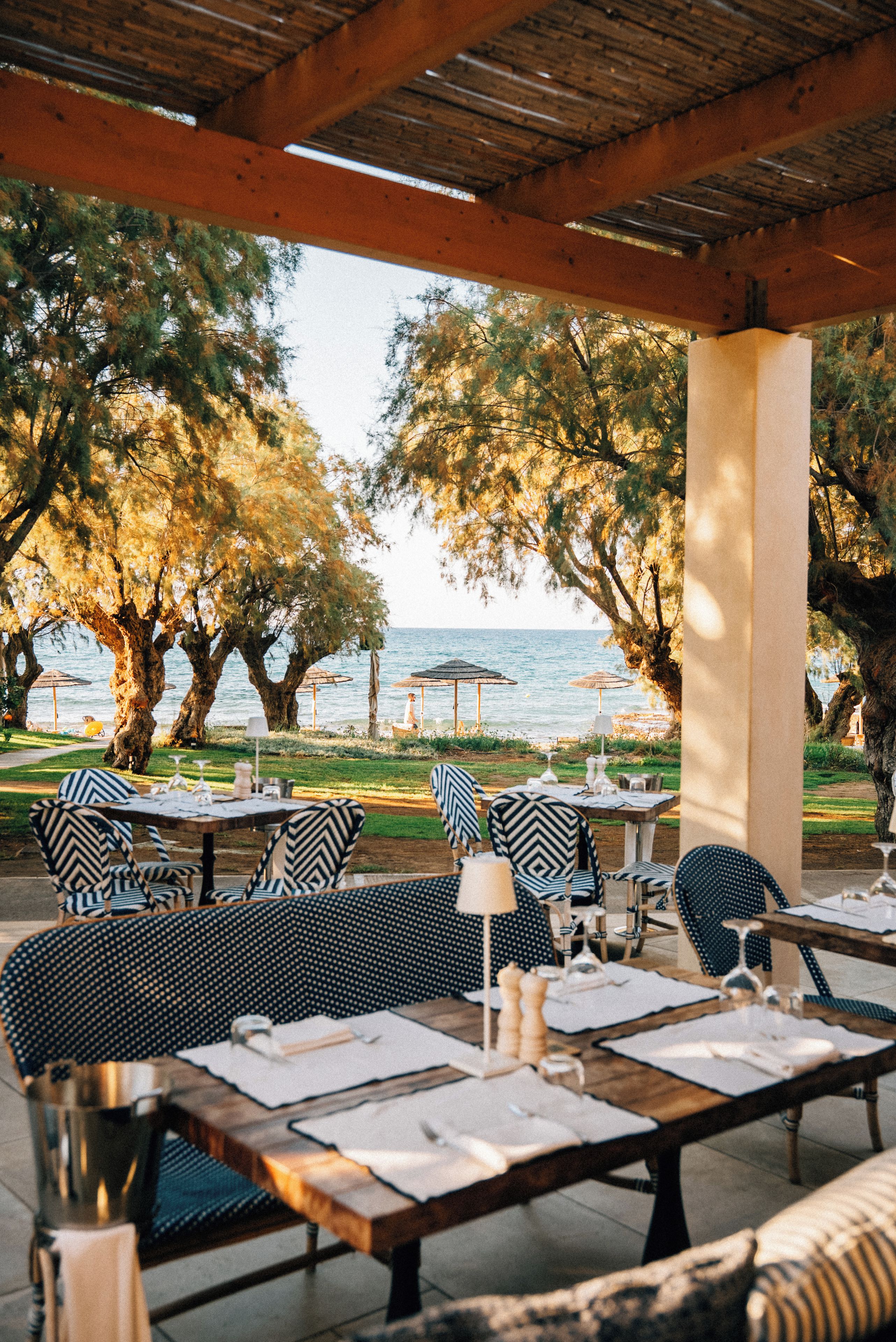 An outdoor dining area with tables and chairs, overlooking a body of water and trees.
