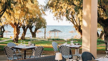 An outdoor dining area with tables and chairs, overlooking a body of water and trees.