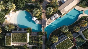 Vue aérienne d’un complexe hôtelier doté de deux piscines, entouré de palmiers et d’espaces de détente.