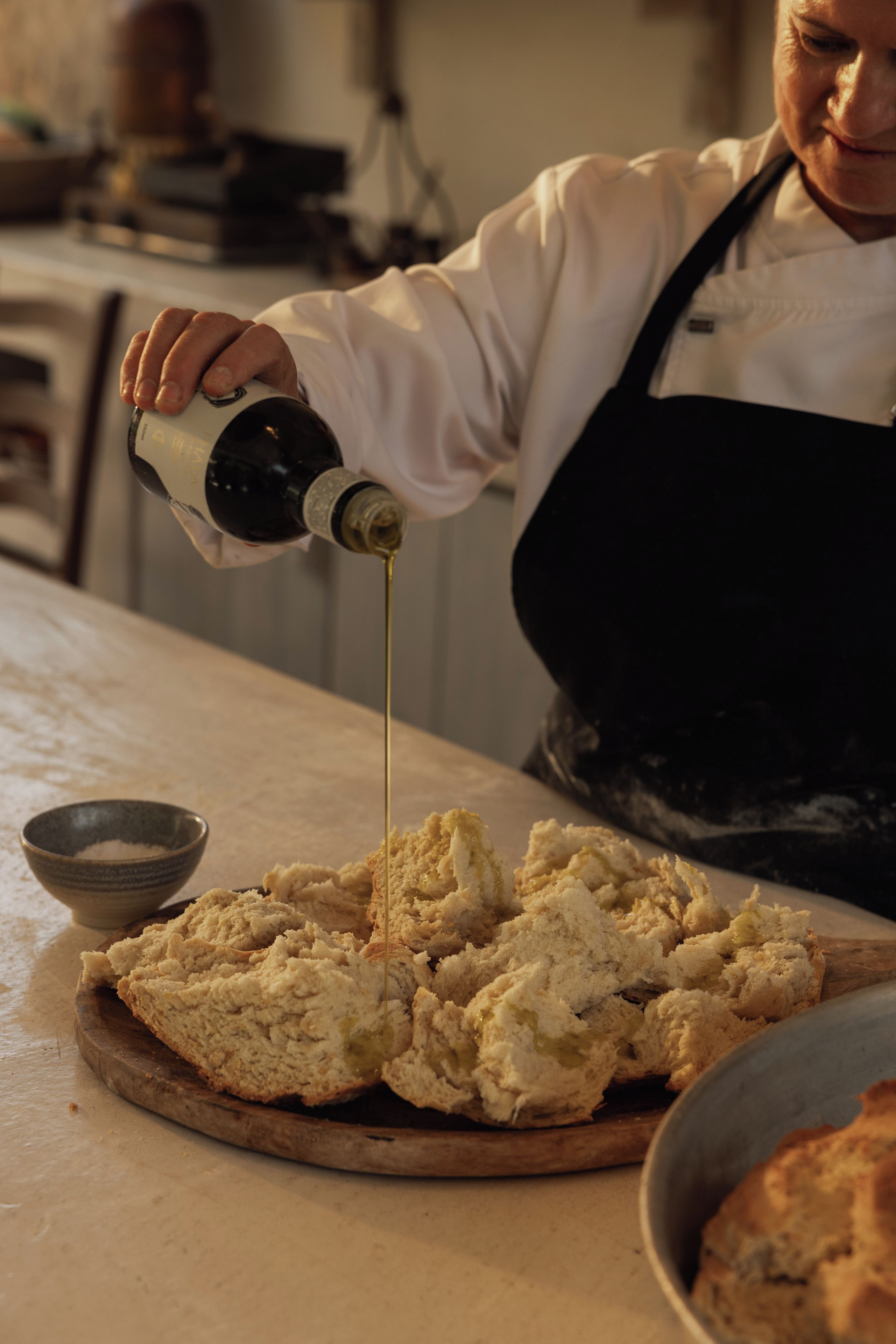 A person pouring a liquid onto a wooden cutting board with bread.