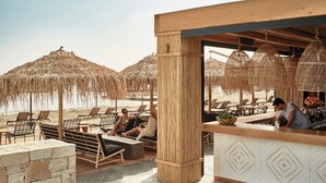 Een terras met rieten parasols, loungestoelen en een bar voorzien van een rieten mand vol fruit.