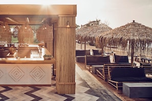 Un espace bar avec un comptoir, des sièges et des parasols en chaume.