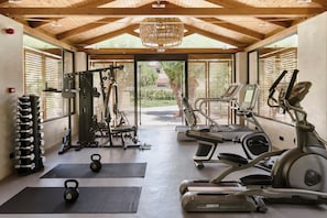 Ein Fitnessstudio mit Laufbändern, Hanteln und Blick auf Grünflächen.