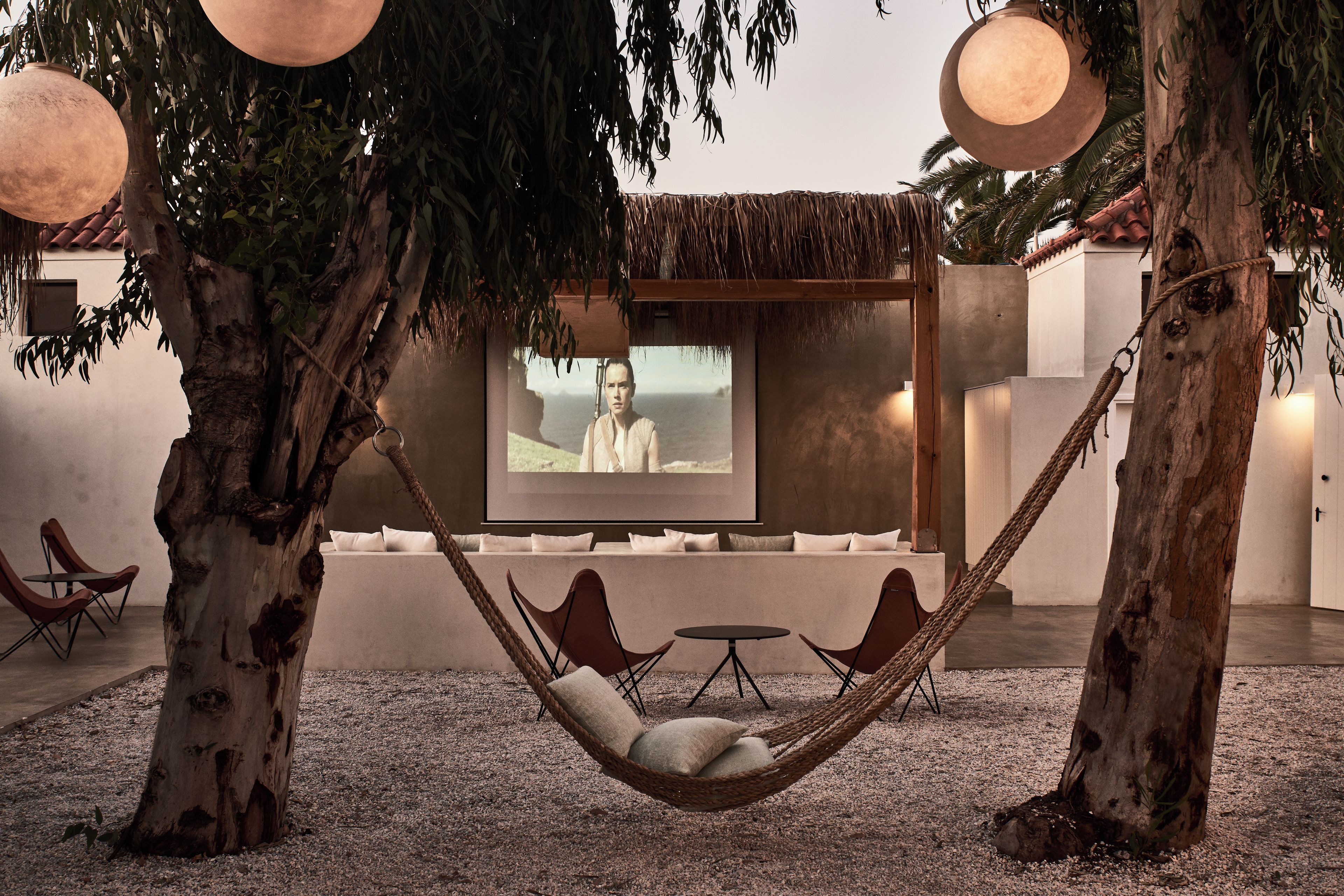 A hammock chair under a tree with a television screen in the background.