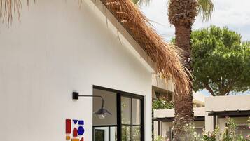 A building with a thatched roof, a palm tree, and a sign reading 'Little Explorers'.