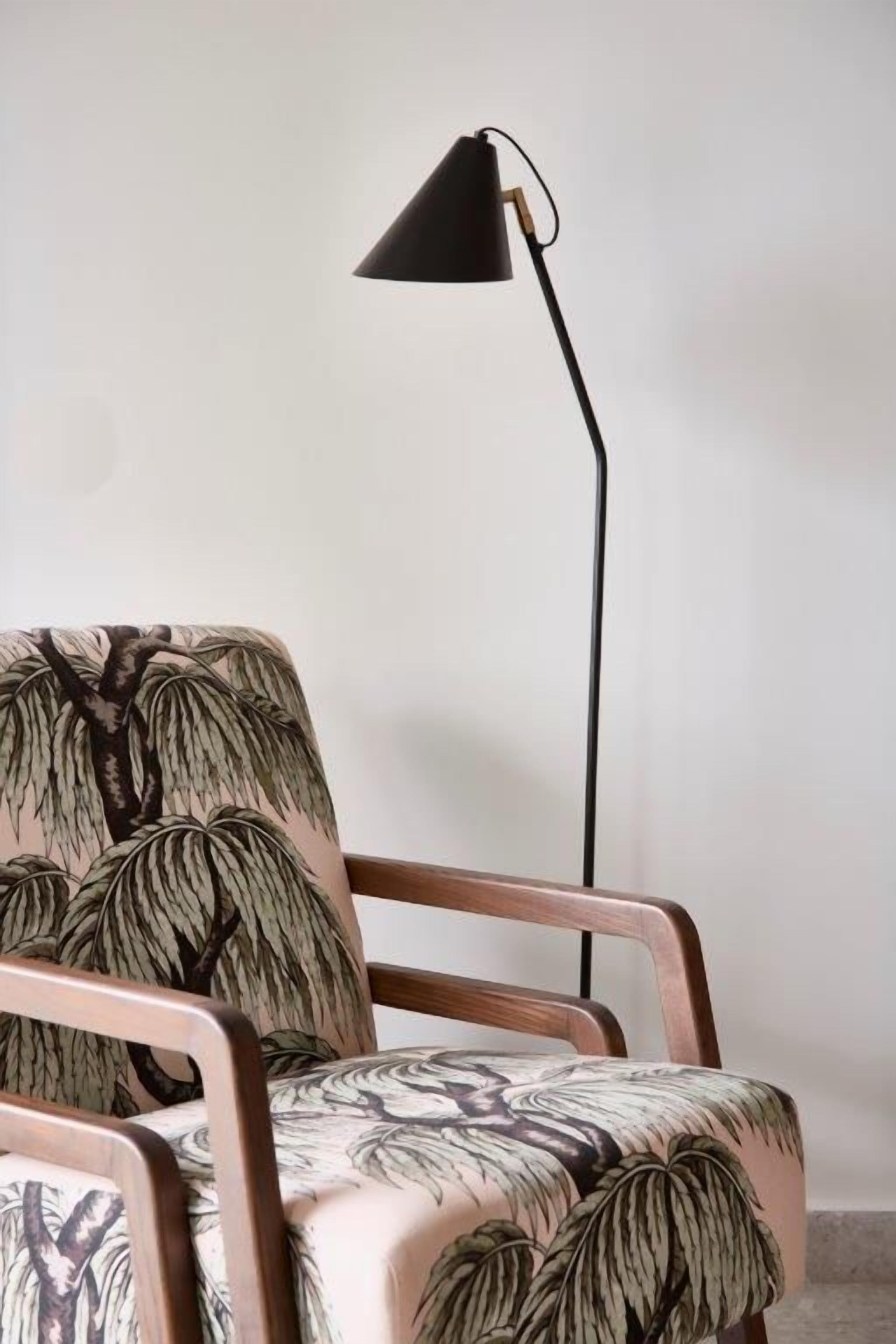 A chair with a leaf pattern upholstery and a black floor lamp beside it.