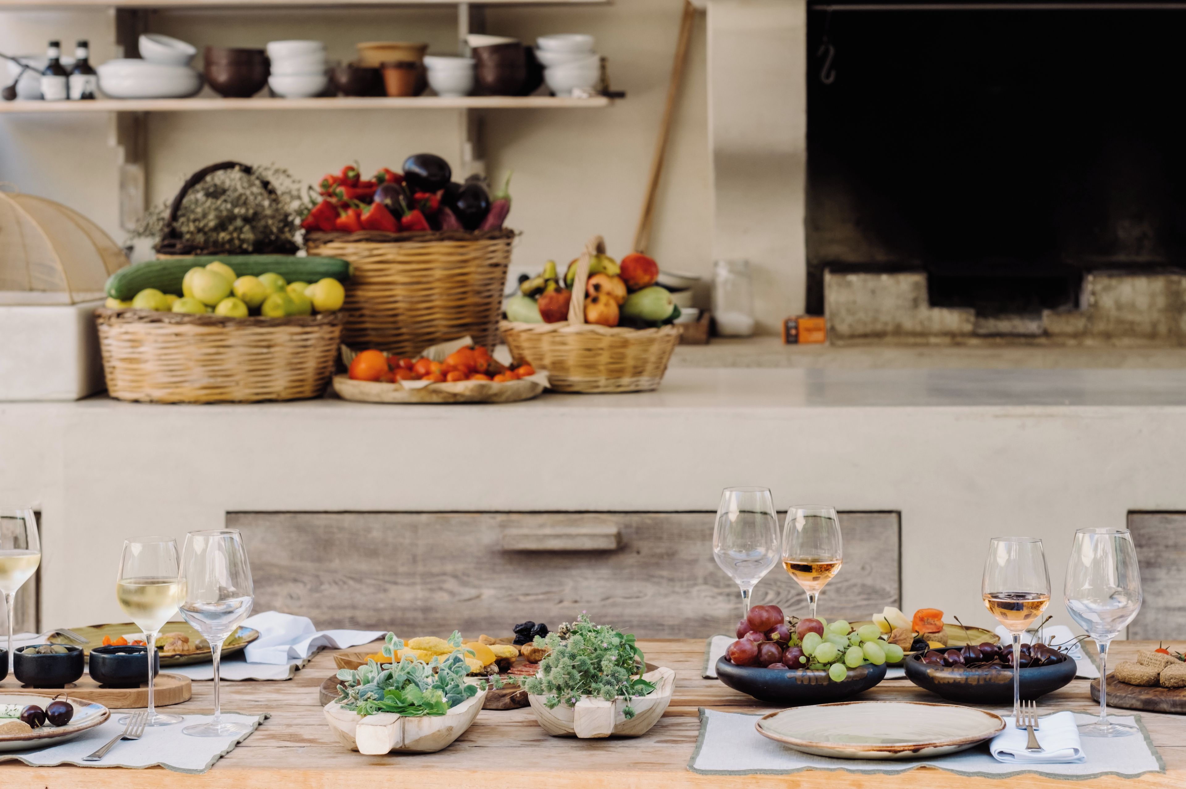 Mesa lista con frutas, verduras y copas de vino, sugiriendo una preparación para la comida.