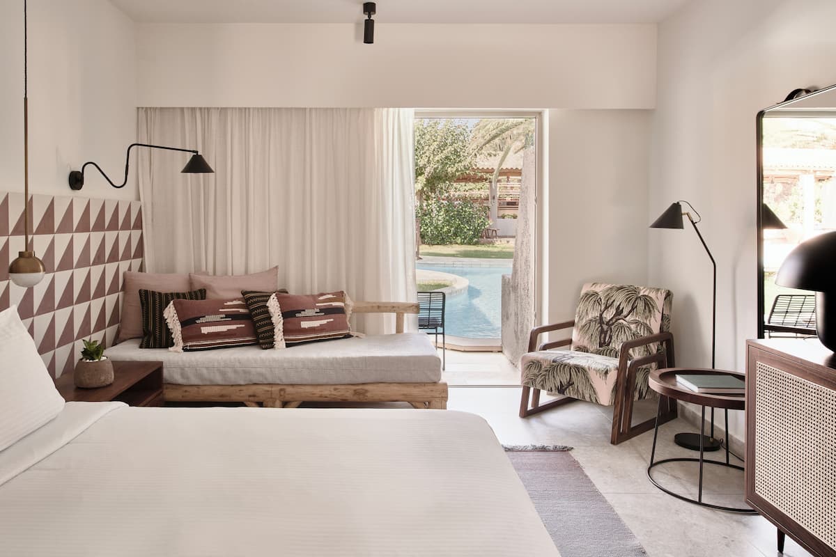 Ein Schlafzimmer mit Bett, Sessel, Schreibtisch und Blick auf einen Swimmingpool.