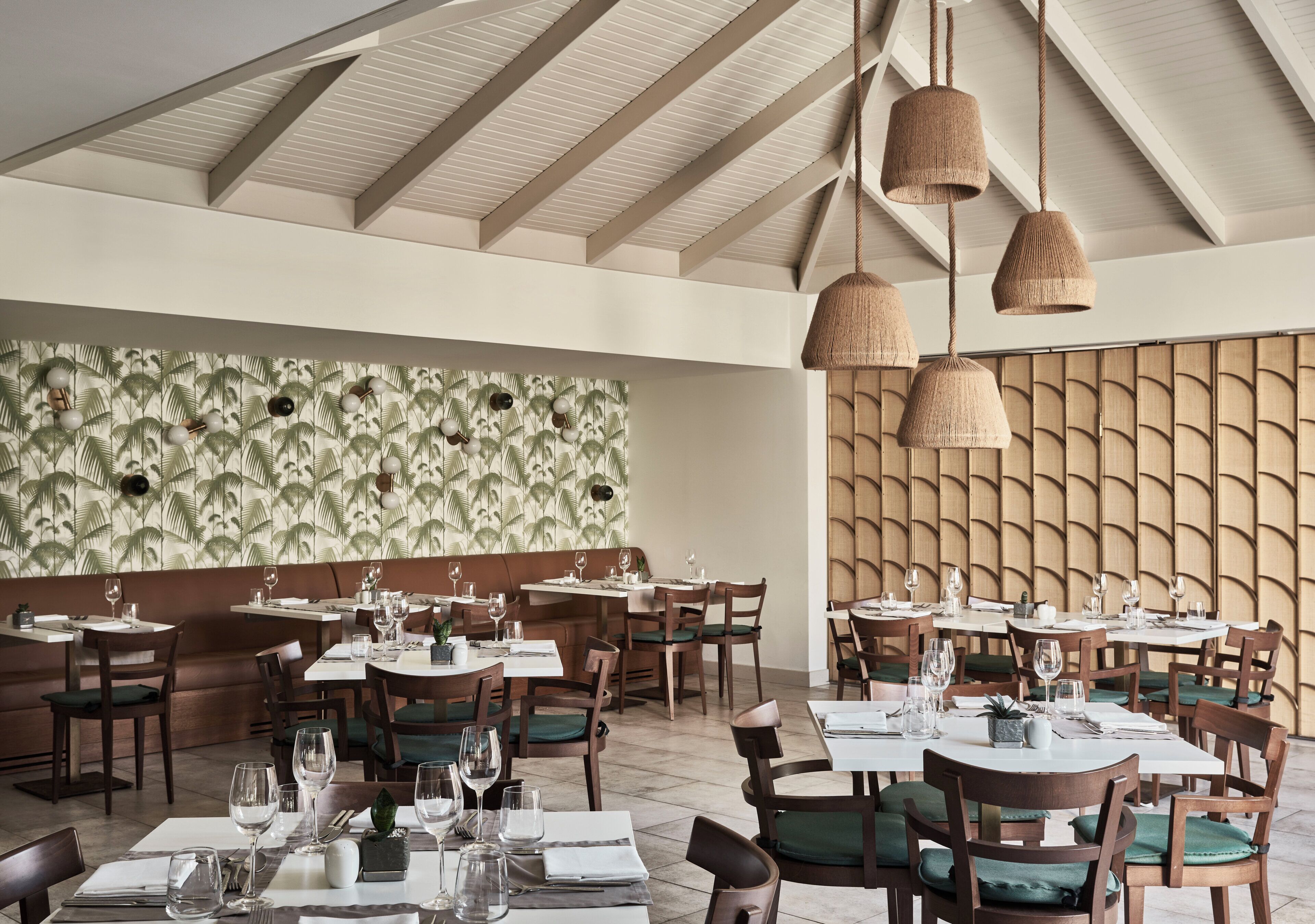 Un restaurante con mesas y sillas de madera, luces colgantes y una pared con diseño.