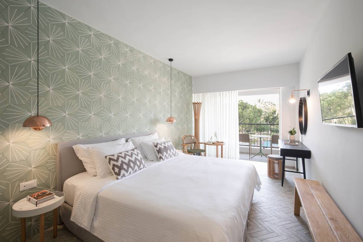 Ein modernes Hotelzimmer mit einem großen Bett, einem kleinen runden Tisch, einer Bank und einem Balkon mit Blick.