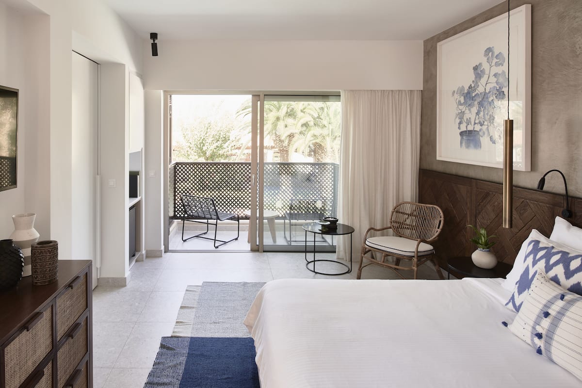 Ein modernes Hotelzimmer mit Balkon, einem Bett, einem Sessel, einem Tisch und einem Bild an der Wand.