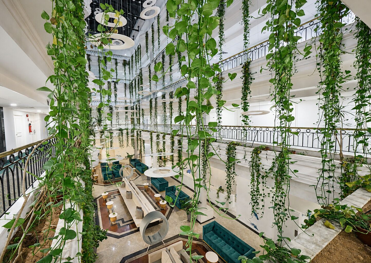 Un amplio atrio con plantas colgantes, una zona de estar central y una escalera.
