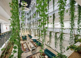 Un amplio atrio con plantas colgantes, una zona de estar central y una escalera.