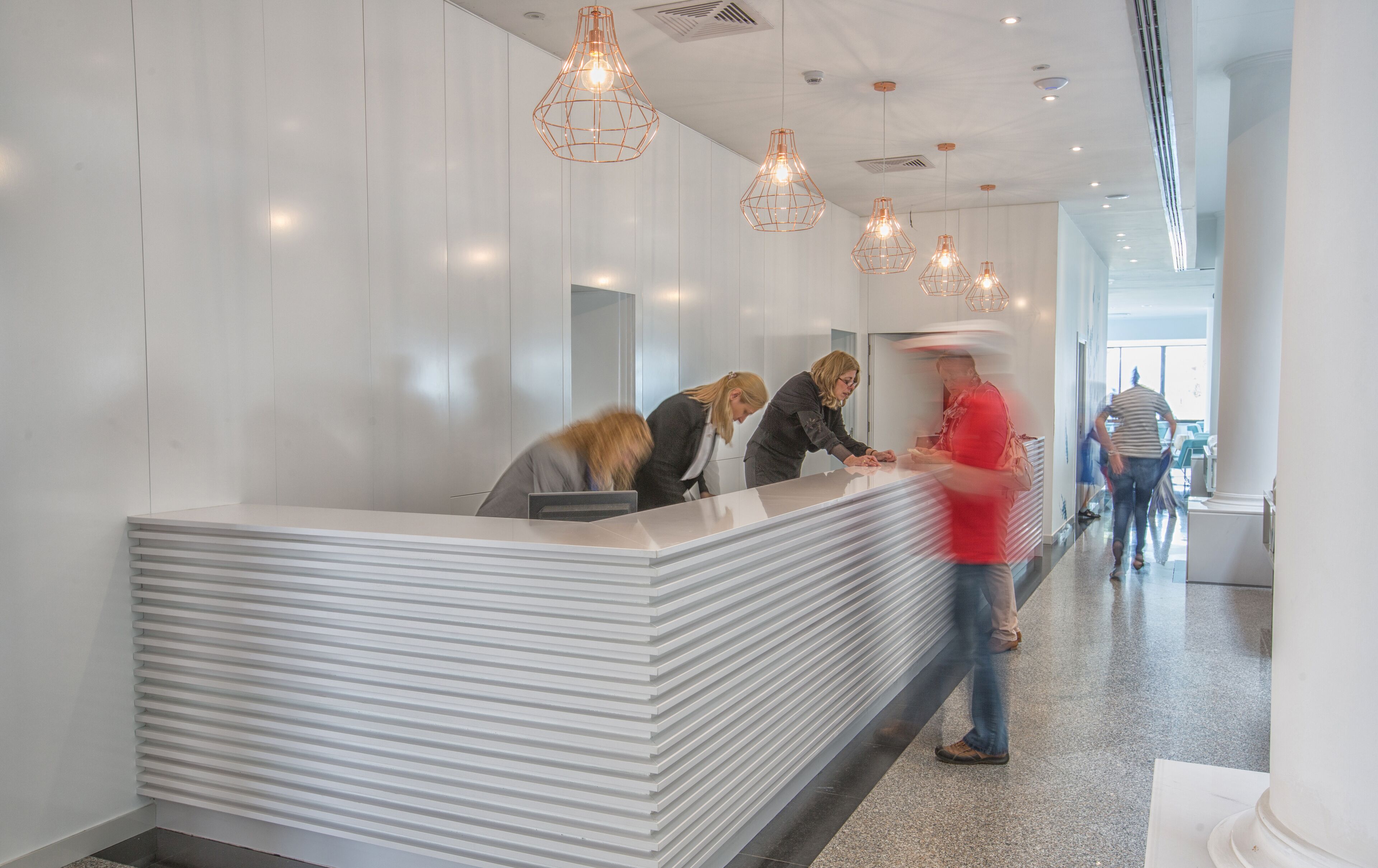 A modern reception area with a white reception desk, multiple pendant lights, and a glass partition.