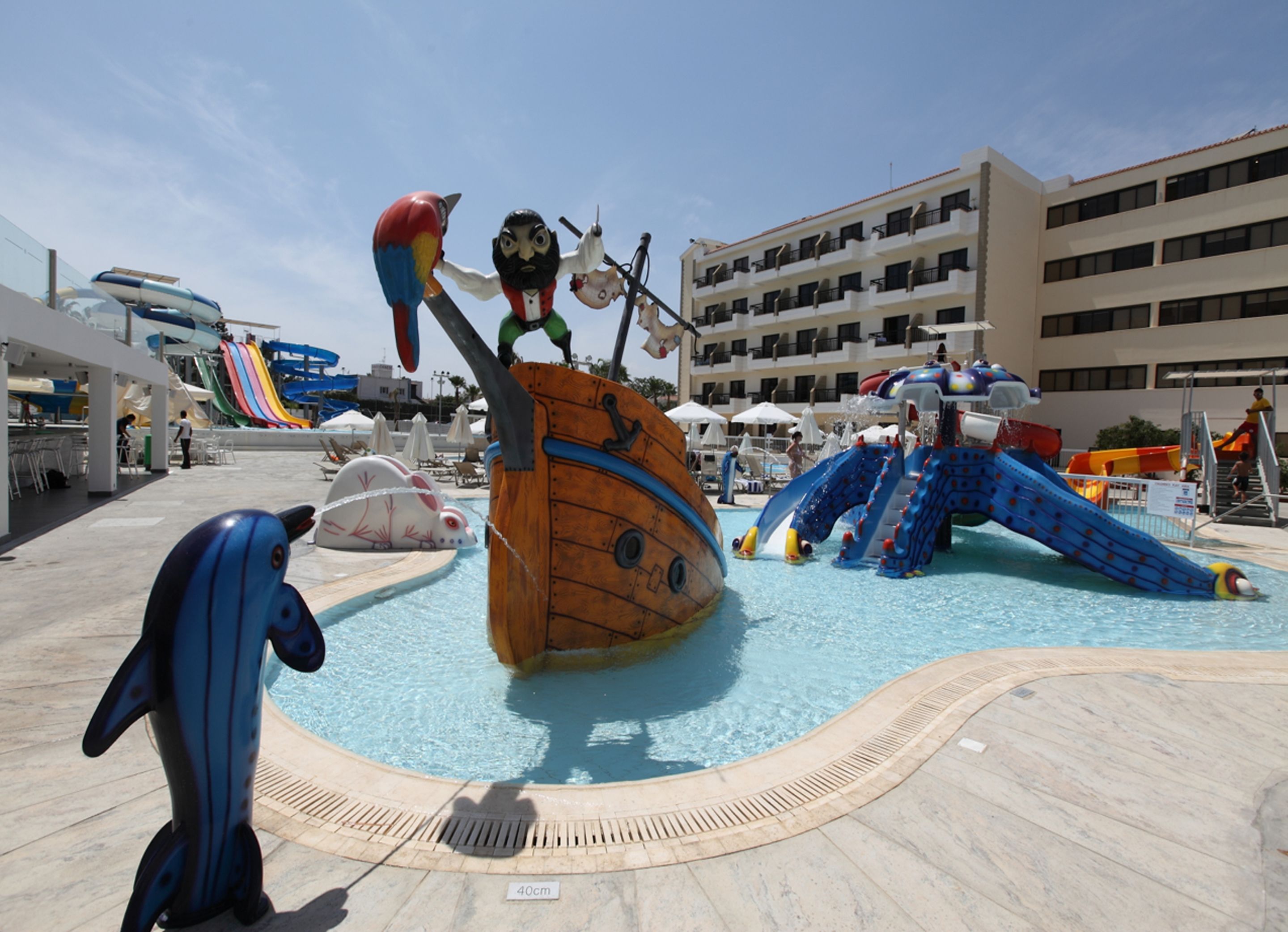 Ein Poolbereich mit einer großen, schiffsartigen Rutsche, einer Delfinstatue und einem Rettungsschwimmturm.