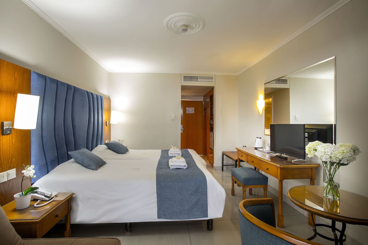 A hotel room with a large bed, a desk, a chair, a TV, and a mirror.